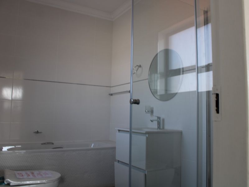 A clean, modern bathroom featuring a bathtub, a vanity unit, and a glass-enclosed shower with white wall tiling.
