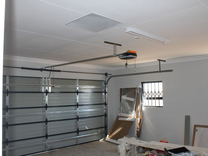 A clean, spacious garage featuring a sectional door, automatic opener, and secure window with burglar bars.