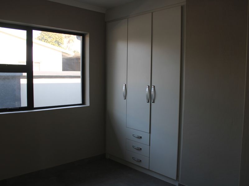 A clean, empty bedroom featuring neutral walls, dark flooring, and modern built-in cupboards with integrated drawers.