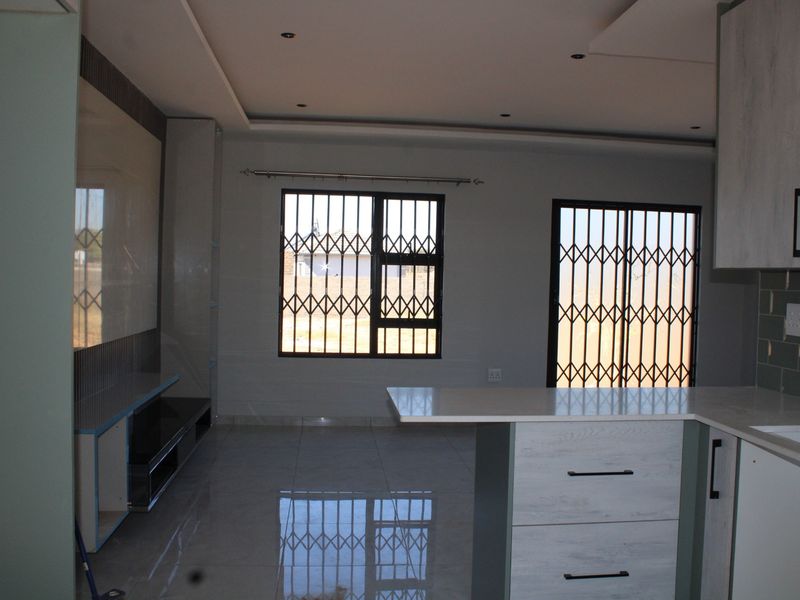 Modern open-plan living and kitchen area featuring sleek cabinetry, a central island, tiled floors, and secure window and door access.