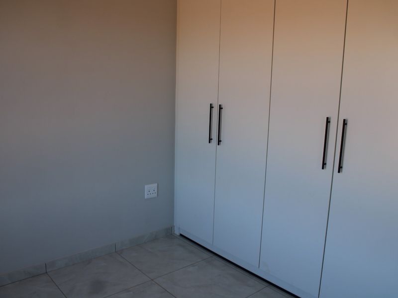 A clean, empty bedroom featuring modern white built-in cupboards and neutral tiled flooring.