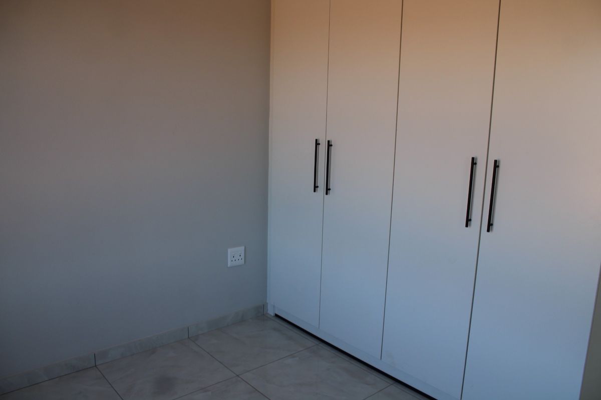 A clean, empty bedroom featuring modern white built-in cupboards and neutral tiled flooring.