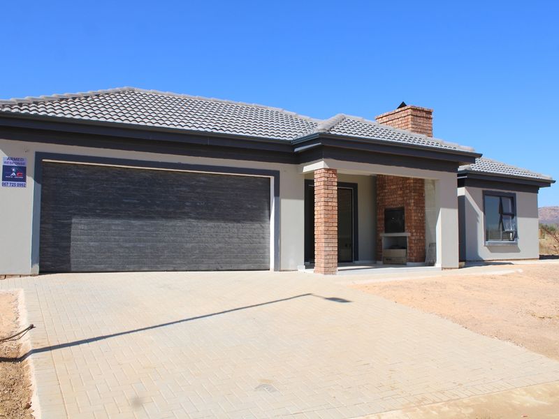 Modern single-story home featuring a tiled roof, paved driveway, automated garage, and a covered patio area with a built-in brick braai.