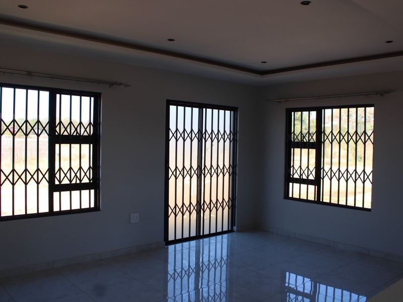 A bright, empty living area featuring tiled floors, recessed ceiling lighting, and secure metal security gates on the windows and sliding door.