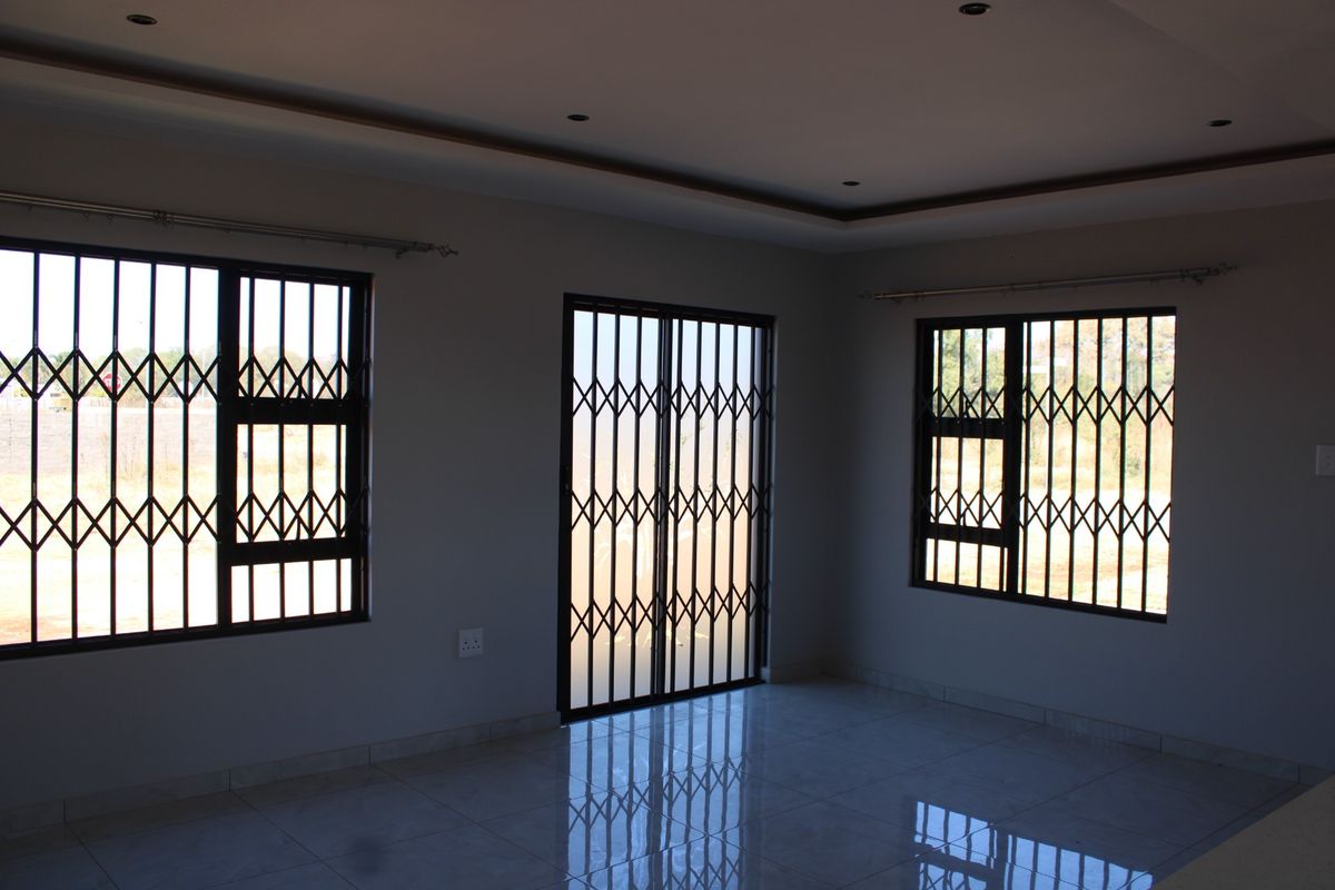 A bright, empty living area featuring tiled floors, recessed ceiling lighting, and secure metal security gates on the windows and sliding door.
