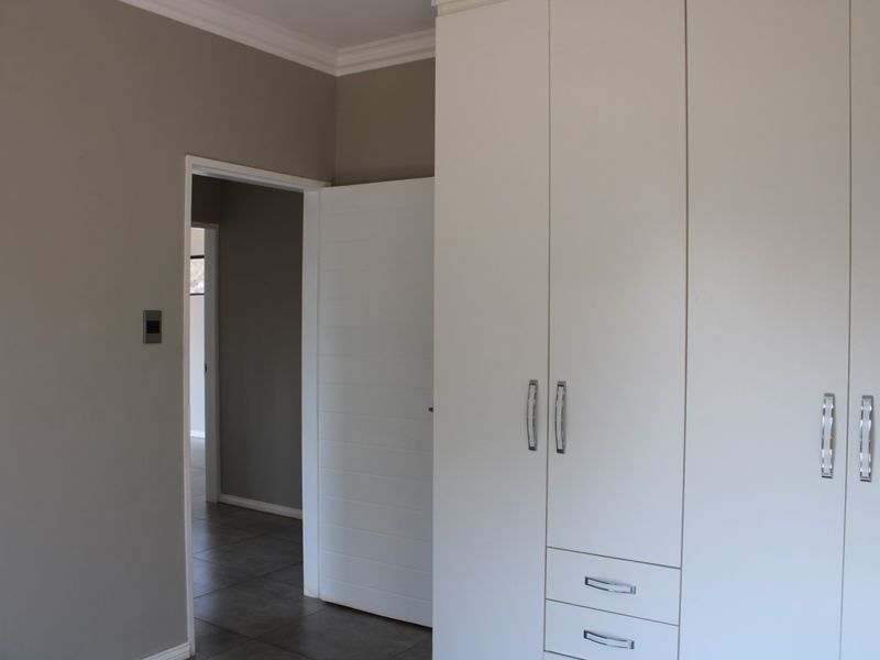 A clean, empty bedroom featuring neutral wall tones, modern tiled flooring, and ample built-in cupboard storage with sleek hardware.