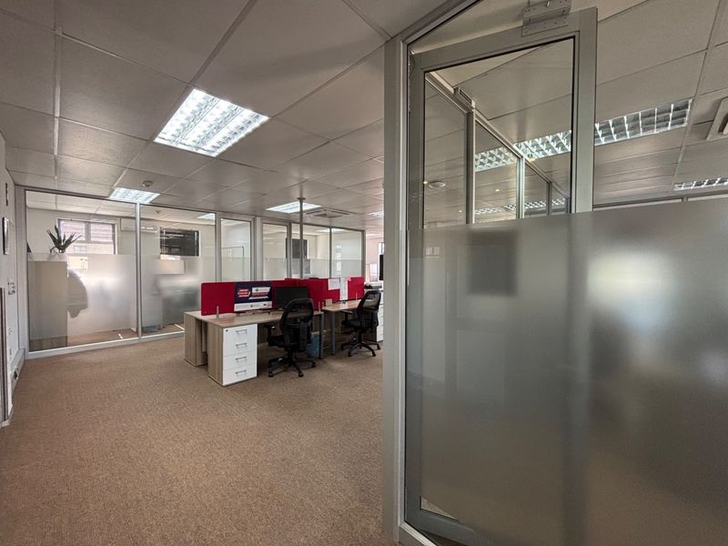 Professional office space featuring glass partition walls, suspended ceilings with recessed lighting, and carpeted flooring, providing a functional and bright work environment.