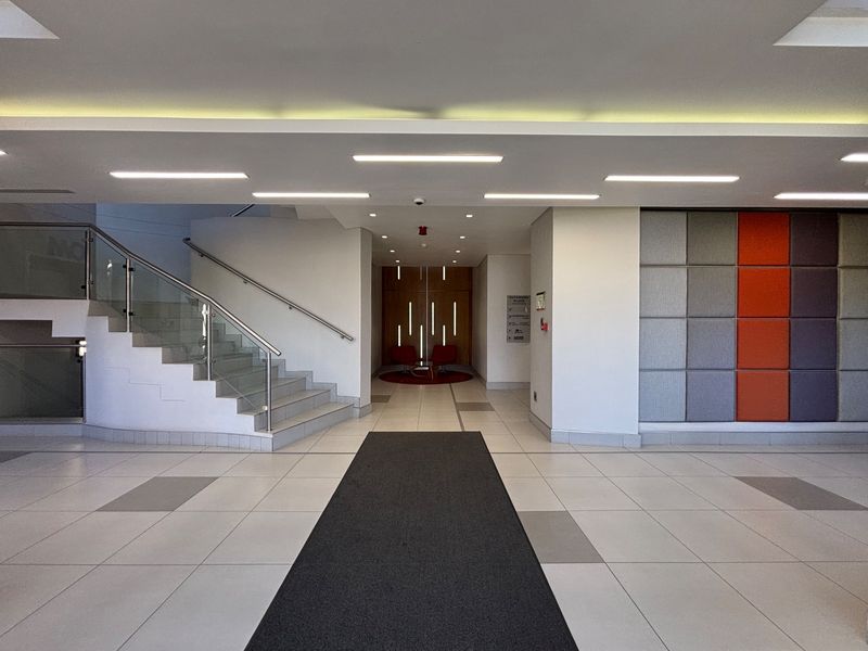 Modern office building lobby featuring tiled flooring, a glass balustrade staircase, and contemporary acoustic wall paneling.
