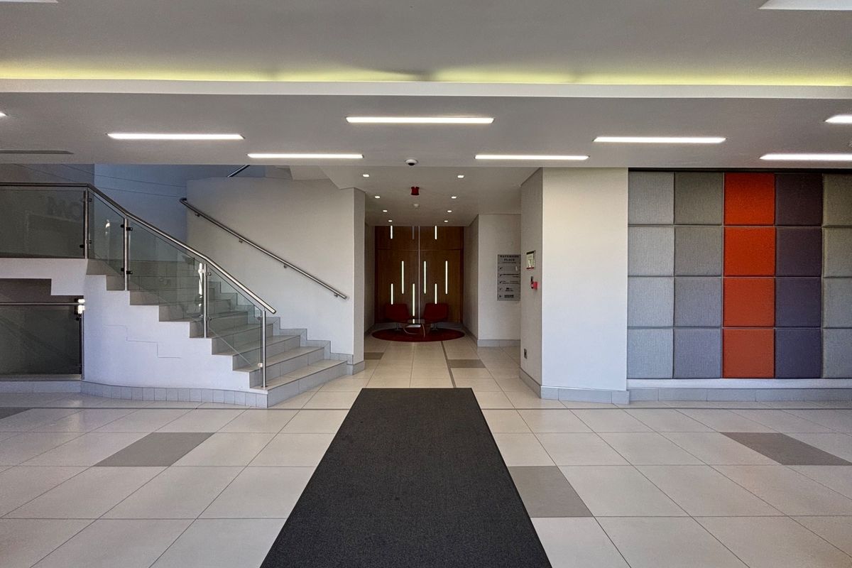 Modern office building lobby featuring tiled flooring, a glass balustrade staircase, and contemporary acoustic wall paneling.