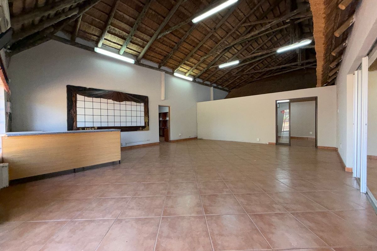 Spacious open-plan office area featuring a high exposed timber thatched roof, tiled flooring, and a built-in reception counter.