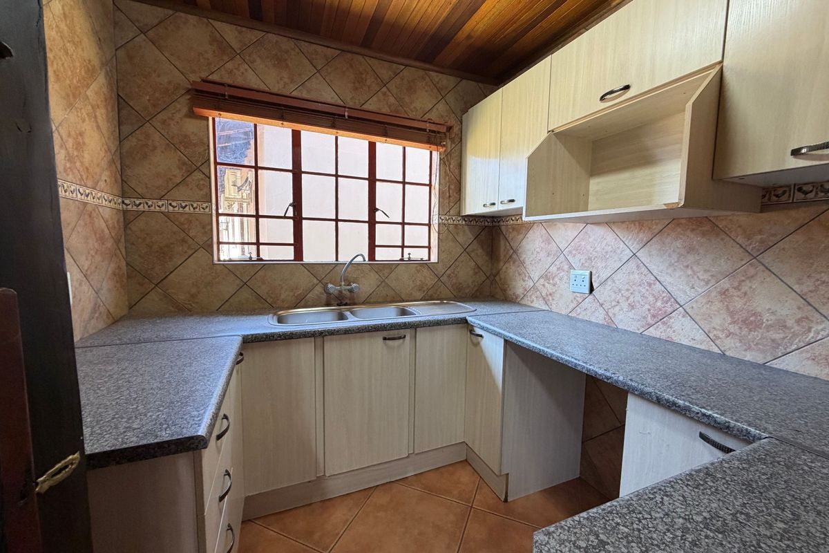 A functional kitchen featuring built-in cabinetry, laminate countertops, a double basin sink, and tiled finishes with a timber ceiling.