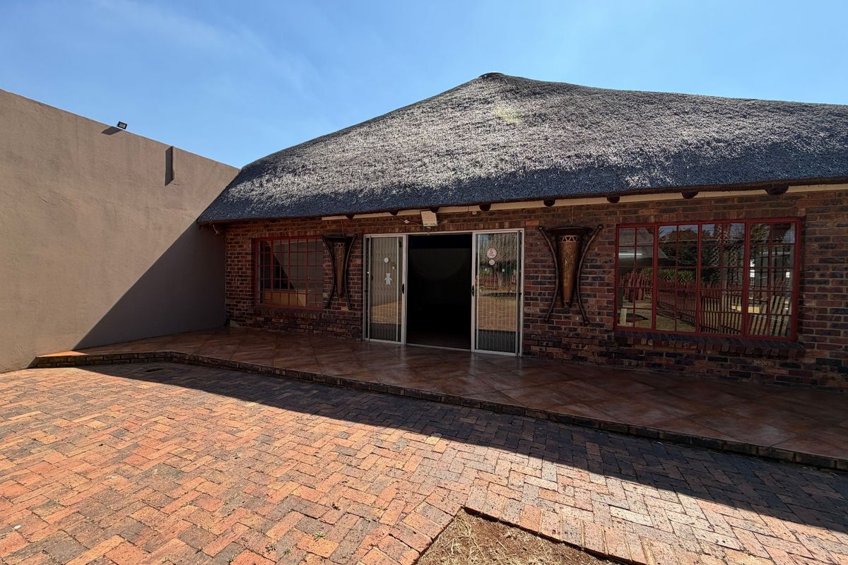 Rear exterior view of a face brick office building featuring a traditional thatch roof, tiled patio area, and paved courtyard.