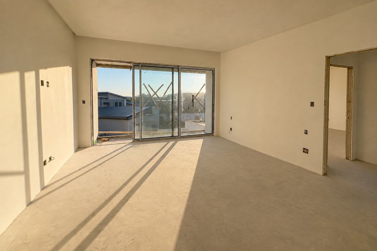 An unfinished interior living space featuring plastered walls, electrical points, and a large sliding glass door leading to an exterior area.