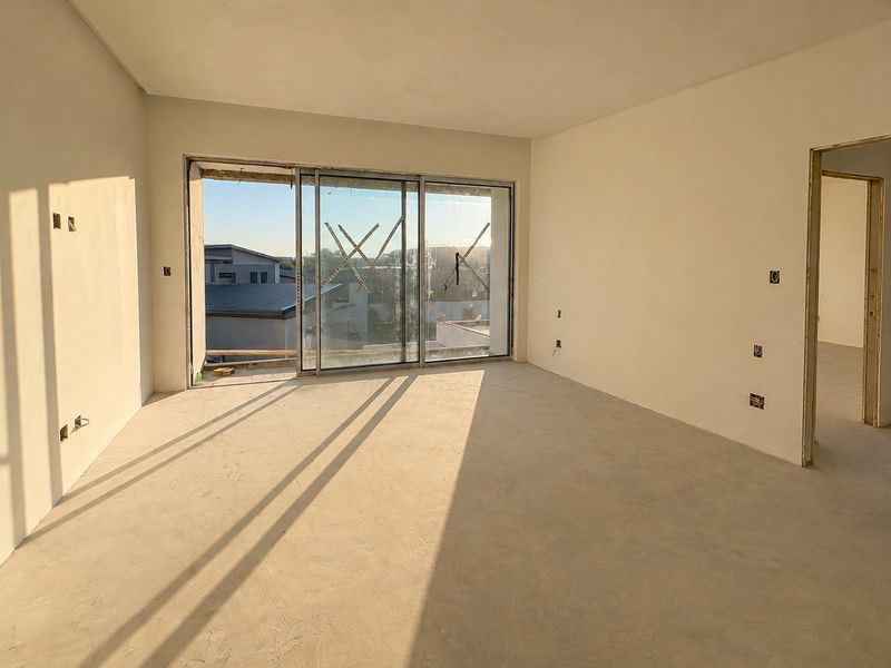 An unfinished interior living space featuring plastered walls, electrical points, and a large sliding glass door leading to an exterior area.