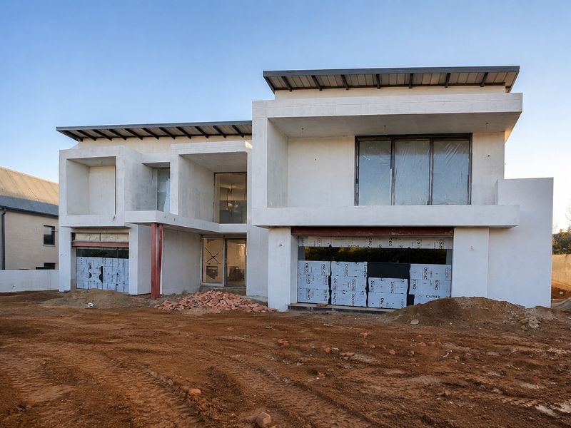 Front elevation of a modern residential property currently under construction, featuring a concrete structure, metal roofing, and large window openings.