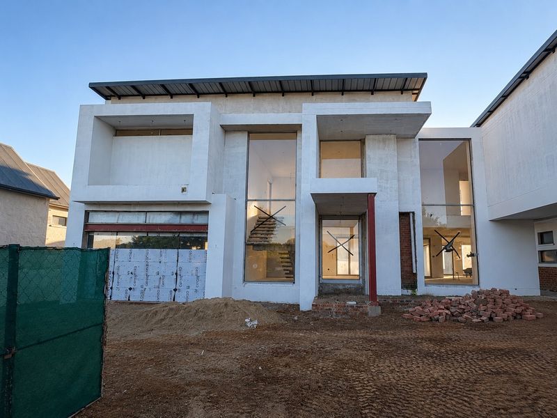 Front elevation of a modern residential property currently under construction, featuring large glass windows and a prominent steel structural beam.