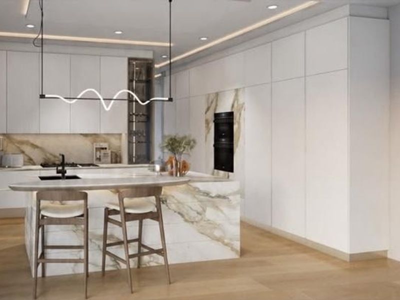 Modern luxury kitchen featuring sleek white cabinetry, a striking marble island with integrated seating, premium built-in appliances, and sophisticated recessed and cove lighting.