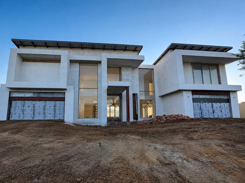 A modern double-story house under construction, featuring a contemporary facade, large glass windows, and a double garage, currently awaiting final landscaping and exterior finishing.