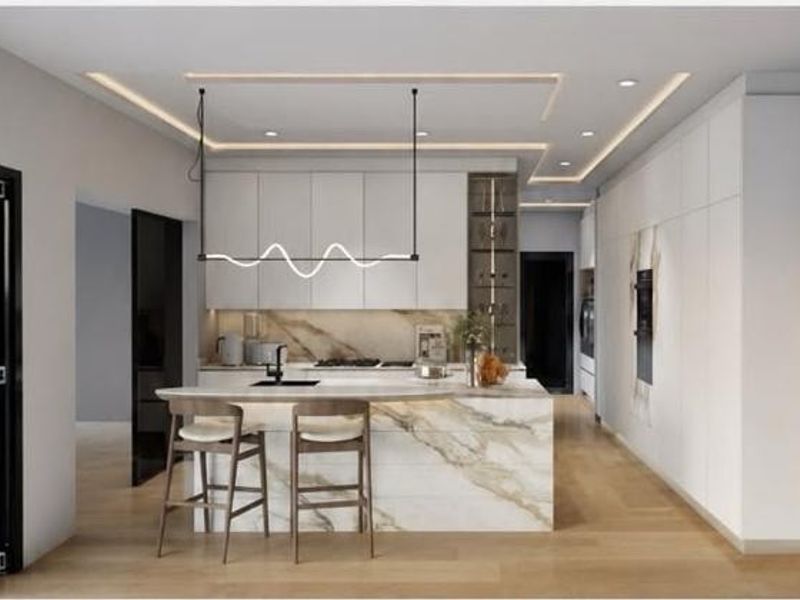 Modern kitchen featuring a marble island, sleek handleless cabinetry, integrated appliances, and recessed ceiling lighting, opening to the outdoors via bi-fold doors.