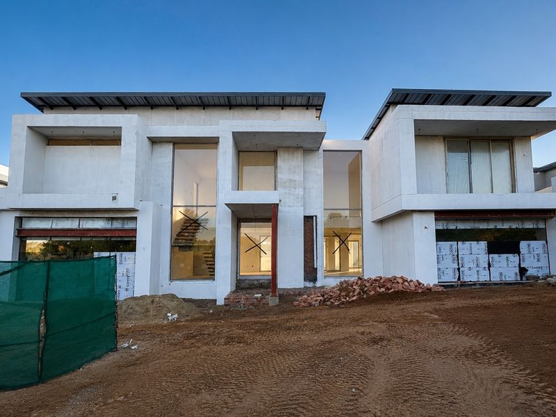 Front elevation of a modern architectural house currently under construction, featuring large glass panels, steel structural elements, and an unfinished exterior facade.