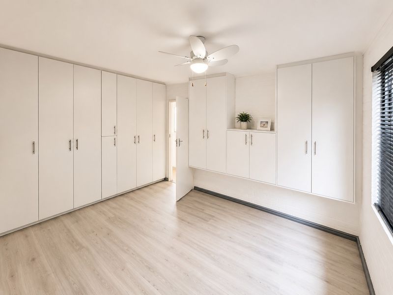 A bright and spacious bedroom featuring extensive built-in cabinetry, modern laminate flooring, and a ceiling fan.