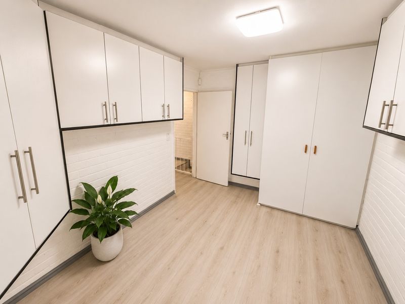 A clean and functional utility space featuring extensive built-in white cabinetry, light wood-look laminate flooring, and painted brick wall finishes.