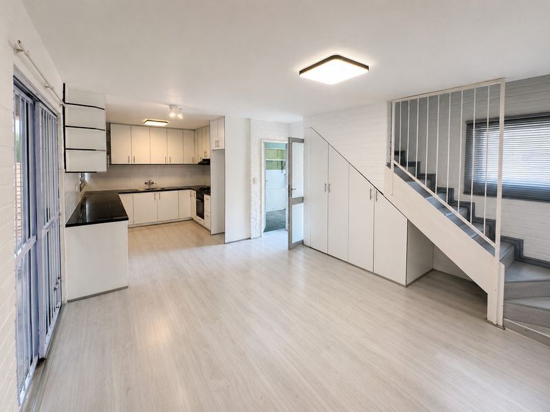 Bright open-plan living area featuring a modern kitchen with black countertops, ample storage, and a staircase with integrated under-stair cabinetry.