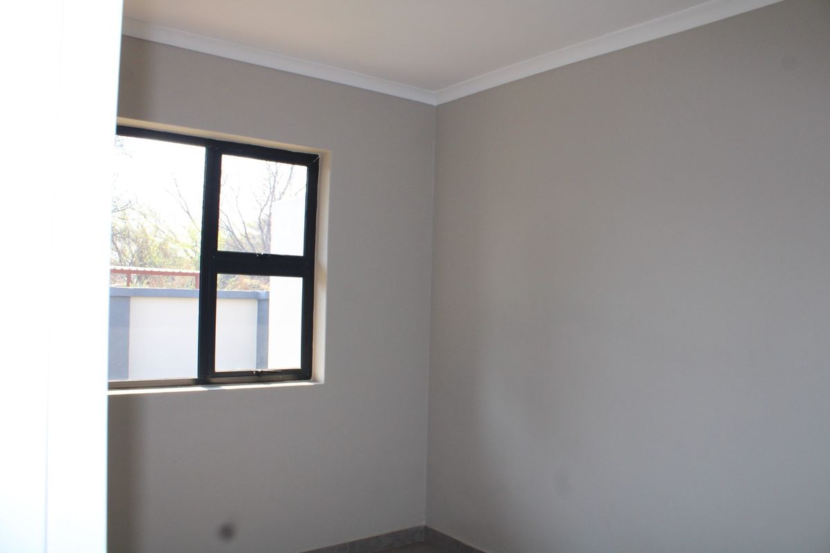 A clean, empty bedroom featuring neutral grey walls, tiled flooring, and a modern black aluminium window frame.
