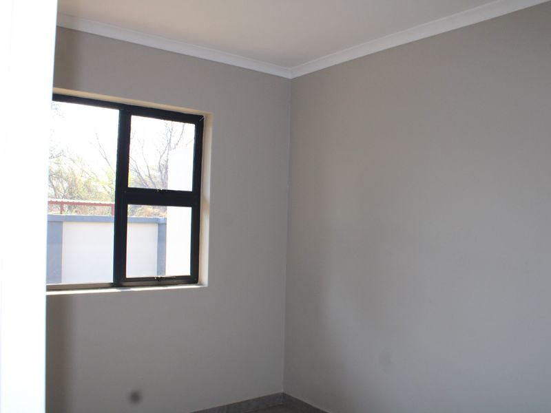 A clean, empty bedroom featuring neutral grey walls, tiled flooring, and a modern black aluminium window frame.