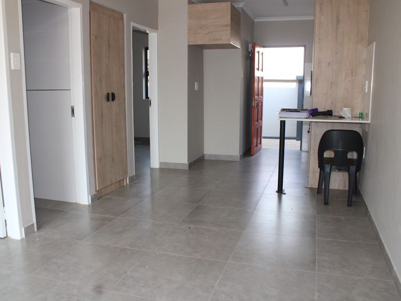 An open-plan living area featuring neutral tiled flooring, modern built-in cabinetry, and direct access to the exterior.