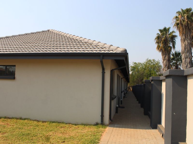 A side view of the townhouse exterior featuring a paved walkway, boundary wall, and tiled roof with integrated guttering system.