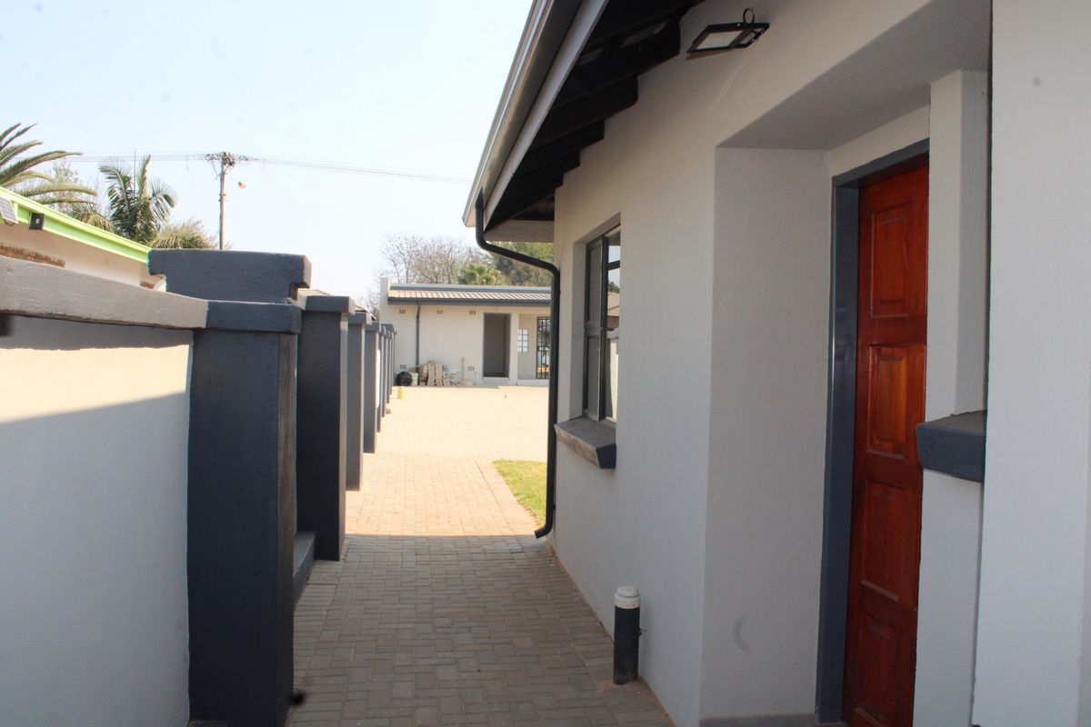 A paved side walkway leading to the rear of the townhouse, featuring a secure boundary wall and exterior access door.