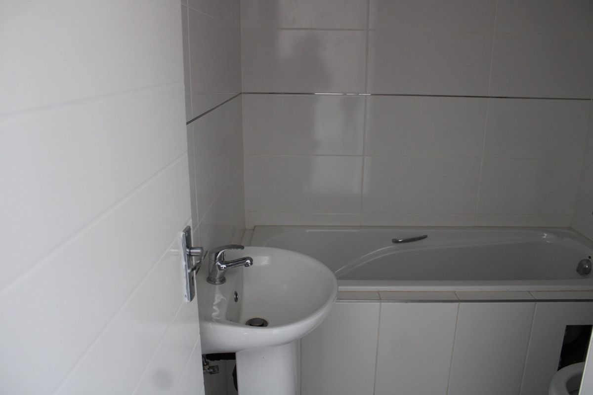 A compact bathroom featuring a white pedestal basin, mixer tap, and a built-in bathtub with neutral wall tiling.