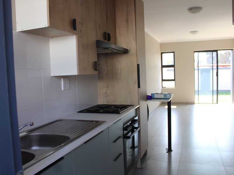 Modern open-plan kitchen and living area featuring contemporary cabinetry, built-in appliances, tiled flooring, and direct access to the rear outdoor space.