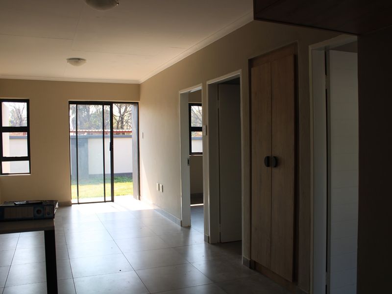 A bright, empty hallway featuring tiled flooring, a built-in cupboard, and a sliding glass door providing access to the rear garden area.