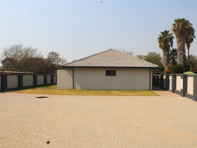 A view of the rear exterior of the townhouse, featuring a paved driveway, perimeter wall, and a tiled roof structure.