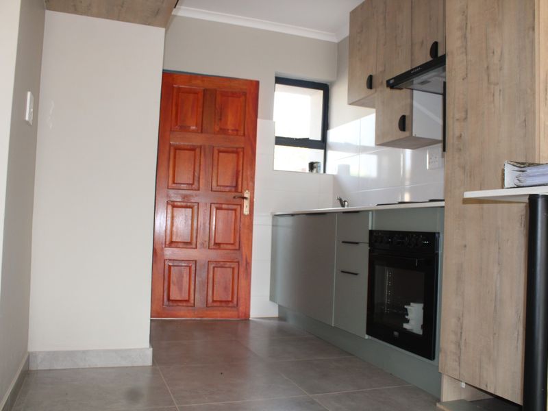 A compact kitchen featuring modern grey cabinetry, built-in oven, extractor fan, tiled flooring, and a solid wood door leading to the exterior.