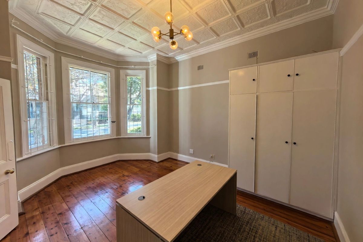 Spacious bedroom featuring a classic pressed metal ceiling, polished timber flooring, a large bay window, and extensive built-in wardrobe storage.