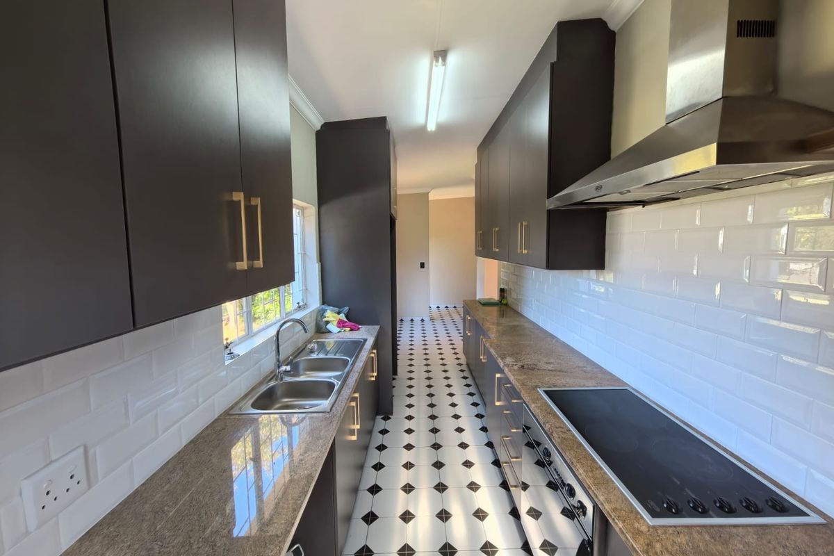 A modern galley-style kitchen featuring dark cabinetry, granite countertops, subway tile backsplash, and integrated appliances with a classic patterned floor.