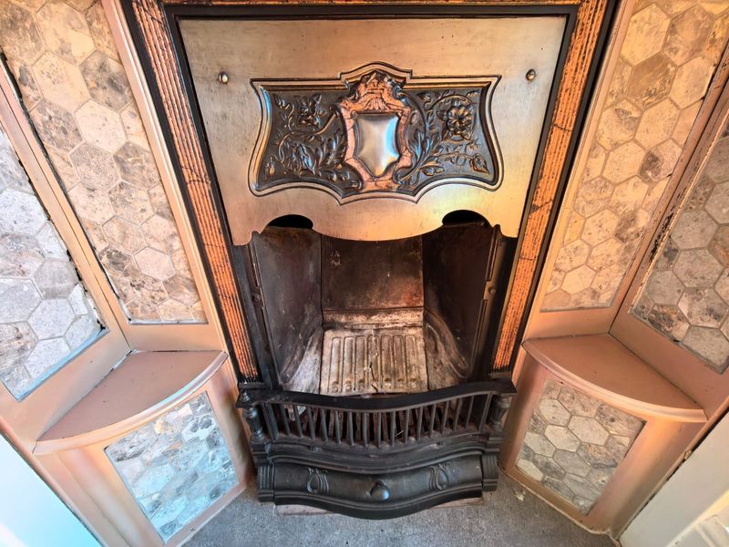 A vintage-style fireplace featuring an ornate cast iron insert and decorative hexagonal mosaic tile surround with integrated corner shelving.