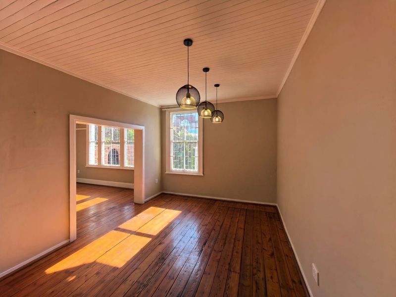 A bright, empty living room featuring original timber flooring, a tongue and groove ceiling, and classic sash windows with natural light.