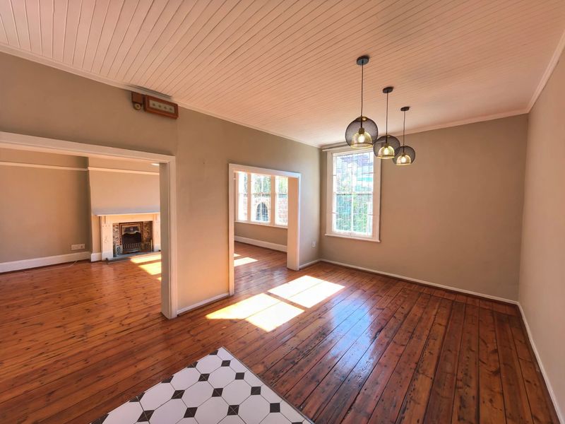 Spacious living area featuring polished timber flooring, a classic beadboard ceiling, and a traditional fireplace, offering a bright and character-filled interior space.