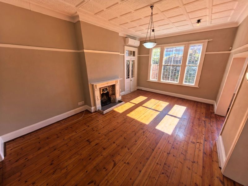 Spacious living room featuring original hardwood floors, an ornate coffered ceiling, and a classic fireplace, offering a bright and character-filled living space.