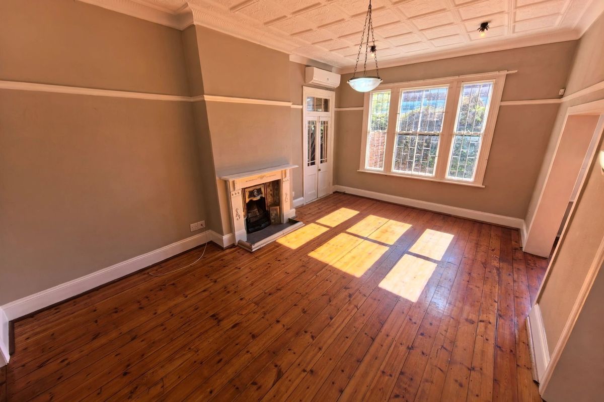 Spacious living room featuring original hardwood floors, an ornate coffered ceiling, and a classic fireplace, offering a bright and character-filled living space.