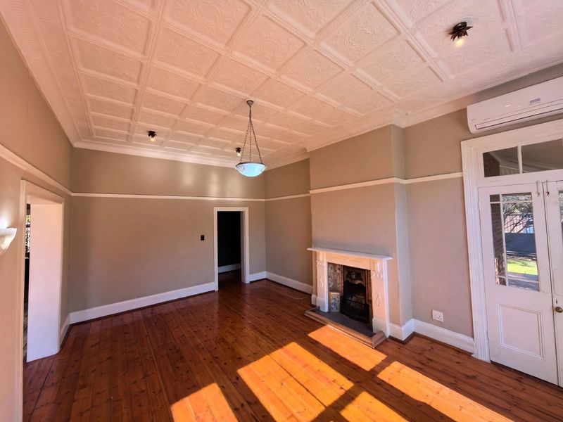 Spacious living room featuring original pressed metal ceilings, polished timber floors, a classic fireplace, and direct access to the exterior via French doors.