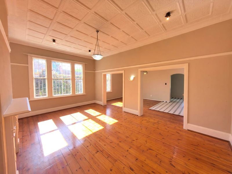 Spacious living room featuring original timber flooring, decorative pressed metal ceilings, picture rails, and charming leaded glass windows with abundant natural light.