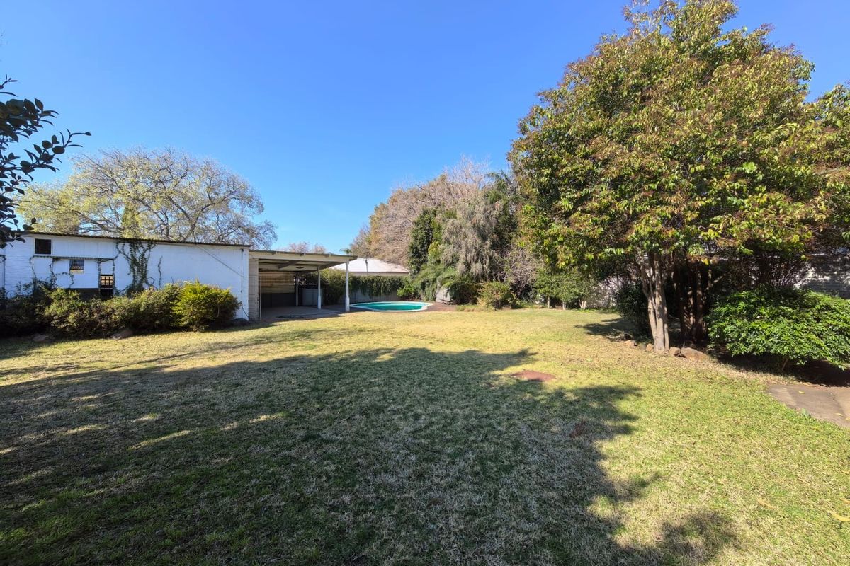 Spacious rear garden featuring a large lawn, mature trees, a swimming pool, and a covered patio area.