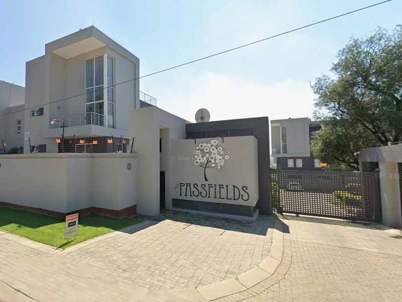 Front entrance view of Passfields apartment complex featuring modern architectural design, secure boundary walls, electric fencing, and a paved driveway.