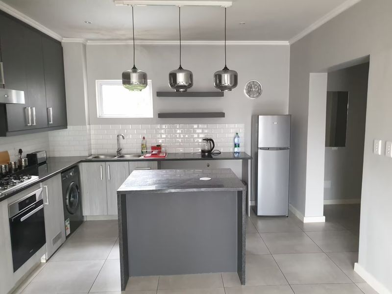 Modern kitchen featuring dark grey cabinetry, a central island, subway tile backsplash, built-in oven, gas hob, and sleek pendant lighting.