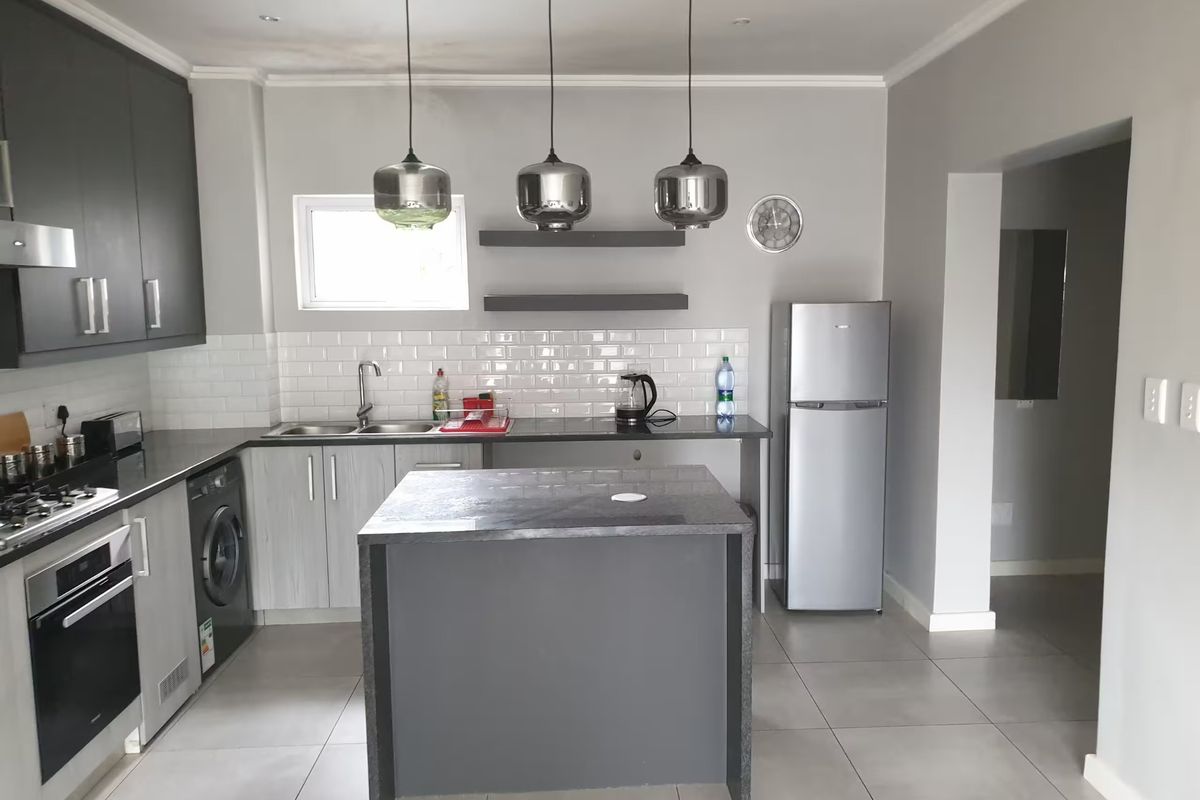 Modern kitchen featuring dark grey cabinetry, a central island, subway tile backsplash, built-in oven, gas hob, and sleek pendant lighting.